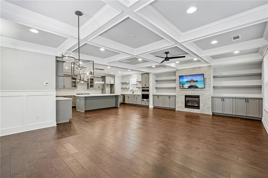 Spacious interior featuring coffered ceilings, rich wood-finish flooring, a modern fireplace with a tiled surround, built-in shelving and cabinetry, and an open-concept kitchen with a large island