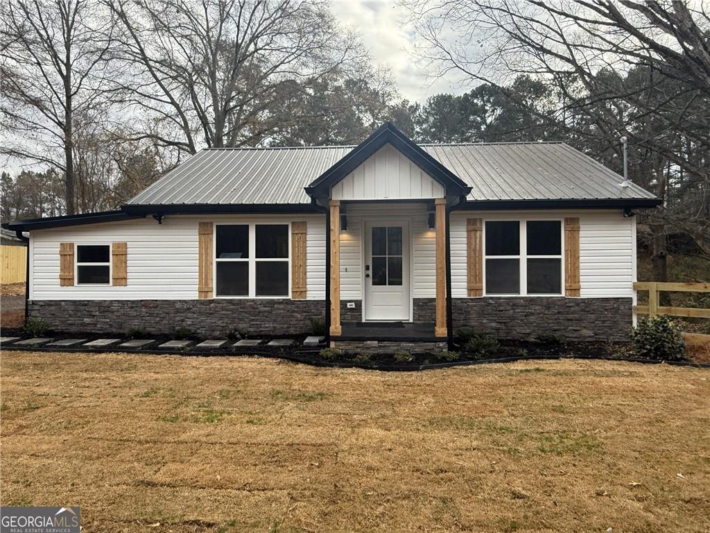 Modern farmhouse-style exterior featuring white siding, a dark metal roof, and stone-look foundation