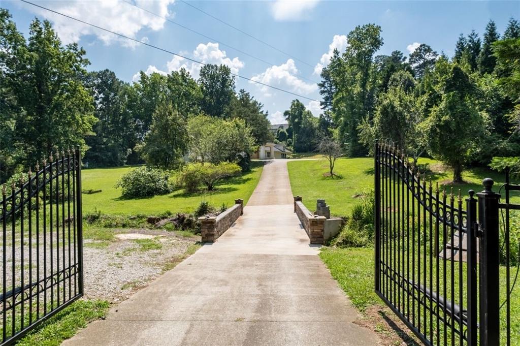 Discover a rare opportunity to own a 6-bedroom, 4.5-bathroom ranch-style estate situated on 2.28 private, gated acres just 2.2 miles from the highly anticipated Gathering at South Forsyth development — the proposed home of a National Hockey League franchise and a vibrant mixed-use destination modeled after The Battery Atlanta. The property includes a 4-bedroom, 3.5-bathroom main residence along with a connected 2-bedroom, 1-bathroom apartment, making it ideal for multigenerational living, guests, or rental income. Inside the main home, the master suite is located on the main level and features an ensuite
bathroom and a creatively designed hidden walk-in closet. Two additional bedrooms and a full bath are also on the main level, while a spacious bonus bedroom with its own full bath is located over the garage. The rest of the main residence consists of a large formal great room, a large office and an open-concept kitchen that flows into a generous living area. The attached apartment features its own private main level living space, along with two upstairs bedrooms and a full bathroom. Outside, the home has wooded surroundings, and it is accessed by a gated driveway that crosses a charming stream via a private bridge. In addition to its immediate appeal as a private residence, this property offers future development potential (ex. a small townhome community). With its proximity to the Gathering at South Forsyth and its 18,000-seat arena, the land is well-positioned. Whether you’re searching for a private retreat, a flexible income-generating property, or an investment opportunity in one of Georgia’s fastest-growing areas, this property offers exciting possibilities.
