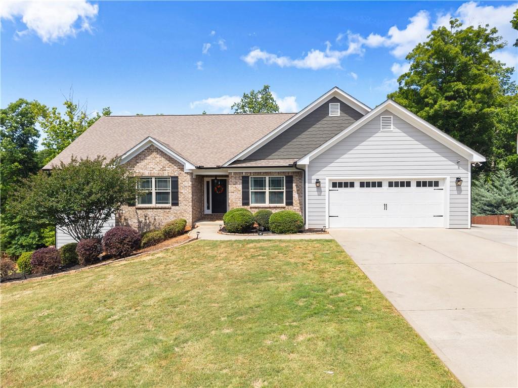 Brick and siding exterior featuring a two-car garage with carriage-style door, concrete driveway, and mature landscaping