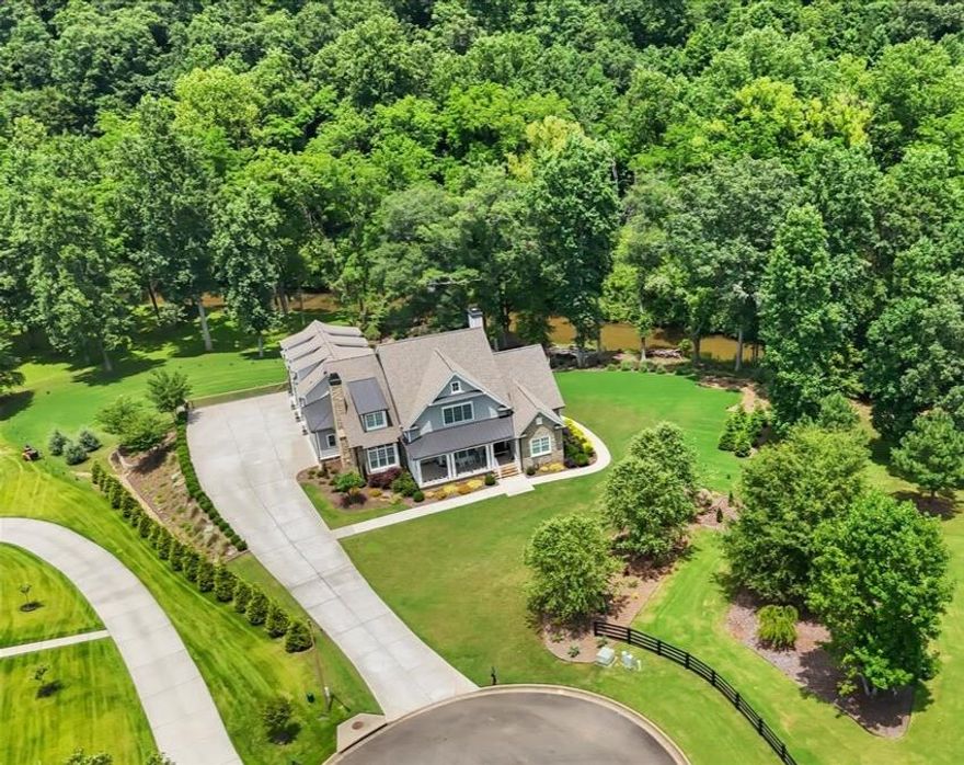 Experience the rare opportunity to own an extraordinary luxury estate, a tranquil masterpiece nestled on two private, park-like acres with stunning frontage on the serene Sharp Mountain Creek. This one-of-a-kind residence is the perfect fusion of natural beauty and refined living, offering an unforgettable setting where the soothing sound of flowing water and complete backyard privacy define the everyday. Tucked away in an exclusive cul-de-sac, this meticulously designed Craftsman-style home presents a sprawling floor plan with 5 spacious bedrooms, 5 full bathrooms, and 2 half baths, reflecting a commitment to luxury finishes throughout.

Step inside to discover timeless elegance and elevated design. The main level features hardwood floors, an open concept layout, and detailed millwork. Walls of windows frame peaceful landscape views. The heart of the home is a chef’s kitchen with custom cabinetry, upgraded GE Monogram appliances, quartz countertops, a large island, farmhouse sink, and a stunning wood-trimmed range hood. This space flows effortlessly into a vaulted keeping room with a stone fireplace, and a grand family room with a coffered ceiling and a second stone fireplace offers additional luxury living space.

The main-level primary suite is a private sanctuary featuring a sitting room and a massive walk-in closet, complete with a spa-like ensuite offering quartz dual vanities, a soaking tub, and an elegant custom-tiled shower. The upper level hosts three thoughtfully designed bedrooms, each with its own ensuite bath, ensuring comfort and privacy. A separate staircase leads to an expansive bonus room, ideal for a home office or playroom.

The fully finished terrace level provides a seamless extension of the home’s living and entertaining space. It includes a second fully-equipped kitchen, an inviting media room, private guest quarters, a fitness room, and a beautifully appointed family room, perfect for sophisticated entertaining.

The backyard is a masterpiece—a tranquil creekside retreat. Enjoy summer evenings gathered around the firepit, soaking in the hot tub, or relaxing on the screened porch—all while overlooking the creek and beautifully manicured grounds. Premium features include a whole-house generator with surge protection, tankless water heater, irrigation system, and a spacious 3-car garage. Located in a top-rated school district with convenient access to the interstate and minutes from the charming downtown Ball Ground.

This is more than a home—it’s a sanctuary where elegance, serenity, and modern luxury unite in perfect harmony. Schedule your private showing today to experience this unparalleled creekside lifestyle!