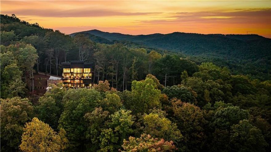 Welcome to 321 Skylight Drive, a rare luxury retreat in the coveted Aska Adventure Area only a short stroll to the Toccoa River and moments from renowned hiking and biking trails and Lake Blue Ridge. Tucked away on a private mountain-view lot with layered long-range vistas and all-paved access, this home blends upscale design with a timeless mountain setting. Step inside and be greeted by soaring cathedral ceilings, walls of glass, and a striking fireplace anchoring the open-concept living space. The gourmet kitchen is designed for entertaining, with commercial-grade appliances, custom cabinetry, and a spacious island that flows seamlessly into a generous dining area. Glass sliders lead to an expansive covered deck, complete with a stone fire table and panoramic views perfect for four-season outdoor living. With five ensuite bedrooms plus a bunk room, every guest enjoys privacy and comfort. The bathrooms are truly spa-like, featuring designer tile, statement lighting, large showers, and in the primary suite, a soaking tub, dual vanities, and a custom walk-in closet with an in-closet laundry station. The terrace level is built for relaxation and entertainment, showcasing a spacious den with fireplace, billiards area, wet bar, and glass doors opening to a stone patio with a heated jacuzzi pool. Every detail in this residence reflects glamorous mountain-rustic luxury, where warm natural textures meet modern sophistication. Sold fully furnished, this exceptional property offers a turn-key investment or private mountain sanctuary in one of North Georgia's most desirable locations.