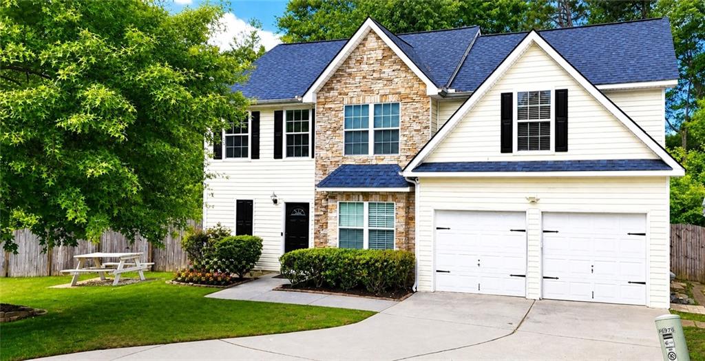 Traditional two-story residence featuring a stone and siding facade, a dark blue shingle roof, a two-car garage, and established landscaping