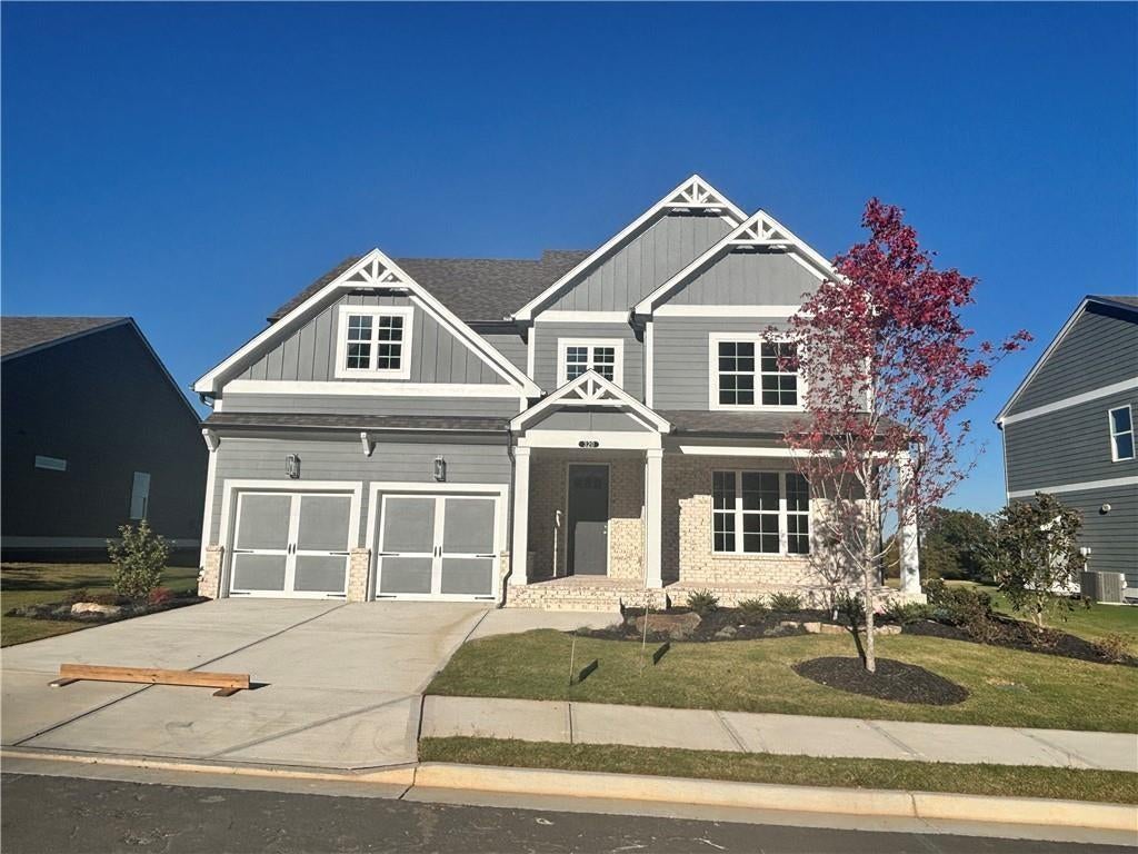Two-story exterior with gray siding, white trim, brick accents, a two-car garage, and a concrete driveway