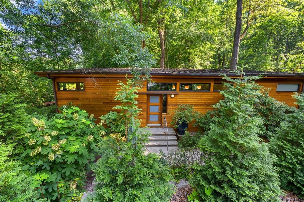 Set back among the trees, this home feels like a serene treehouse, surrounded by nature. This stunning two-story residence offers an inviting and scenic living experience. This property, built in 2007, sits on the foundation of a building constructed in 1915. Due to Atlanta's 75-foot stream buffer regulation, the house occupies its original footprint. The main level boasts large glass windows that provide breathtaking views of an old lake, which was drained in 1930. The dam built for this purpose is still visible, with water flowing from a capped spring 200 yards east, past Fernbank Museum, through the Emory campus, and eventually joining the Chattahoochee River and the Gulf of Mexico. Located near the subcontinental divide, water on the other side of the nearby train tracks flows into the Atlantic.
The heart of the home features an open floor plan that seamlessly combines the kitchen, dining, and living areas, all flooded with natural light from the numerous windows. On the right side of the main level, you'll find the primary suite, complete with an ensuite bathroom featuring a double vanity and glass shower. The left side of the home includes a half bathroom, a second bedroom suite with a daybed and an ensuite bathroom with a tub-shower combo, as well as a home office with a Murphy bed.
Descending a spiral staircase to the second level, you'll find ample storage and laundry facilities, along with the entrance to a separate unit, added in 2023. This beautiful unit includes its own full kitchen, living area, bathroom, laundry, and a flex room with a desk and pull-out sofa. A bed can be arranged upon request, making this suite perfect for a nanny, assistant, guest, or as a private retreat. It has its own entrance and outdoor terrace for added convenience.
Located in the charming Lake Claire neighborhood, this home borders Candler Park, Druid Hills, and Decatur, offering a prime intown location with easy access to all the amenities these areas provide. Lake Claire is a close-knit community known for its friendly neighbors, beautiful parks, and vibrant local culture. Candler Park, just next door, is renowned for its lush green spaces, playgrounds, and the iconic Candler Park Golf Course. Both neighborhoods offer a variety of dining, shopping, and entertainment options, making this an ideal location for those who appreciate a blend of urban convenience and natural beauty.