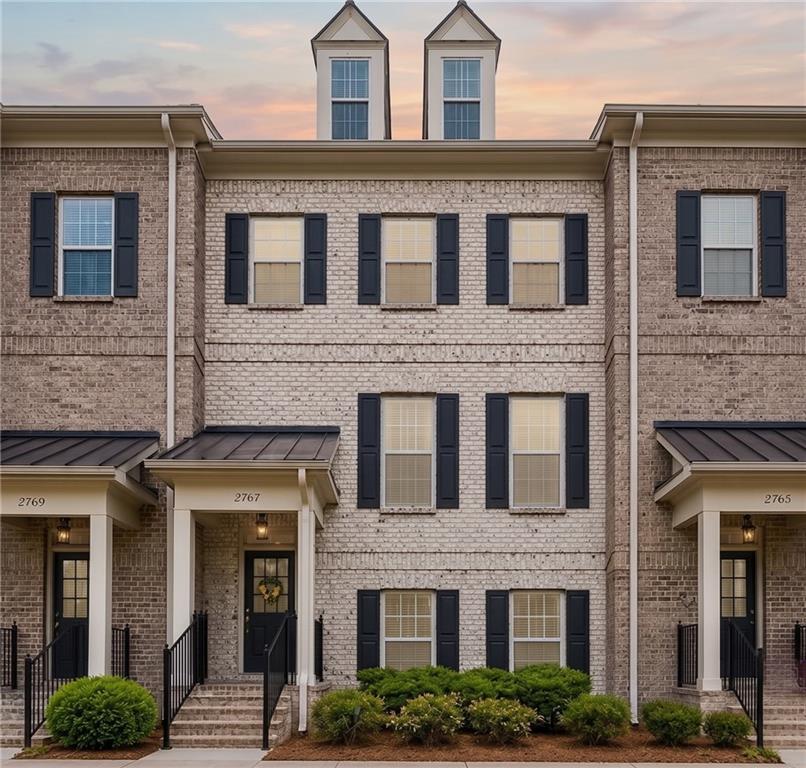 Brick exterior townhome with black window shutters, a covered entry, black metal railings, and dormer windows
