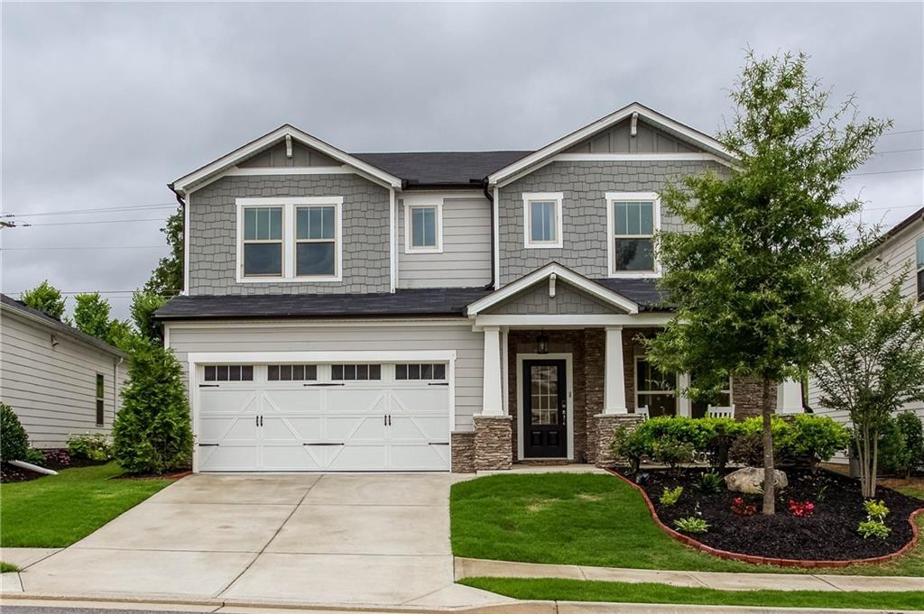 Two-story residence featuring a gray and white exterior with stone accents, a covered front porch, and an attached two-car garage