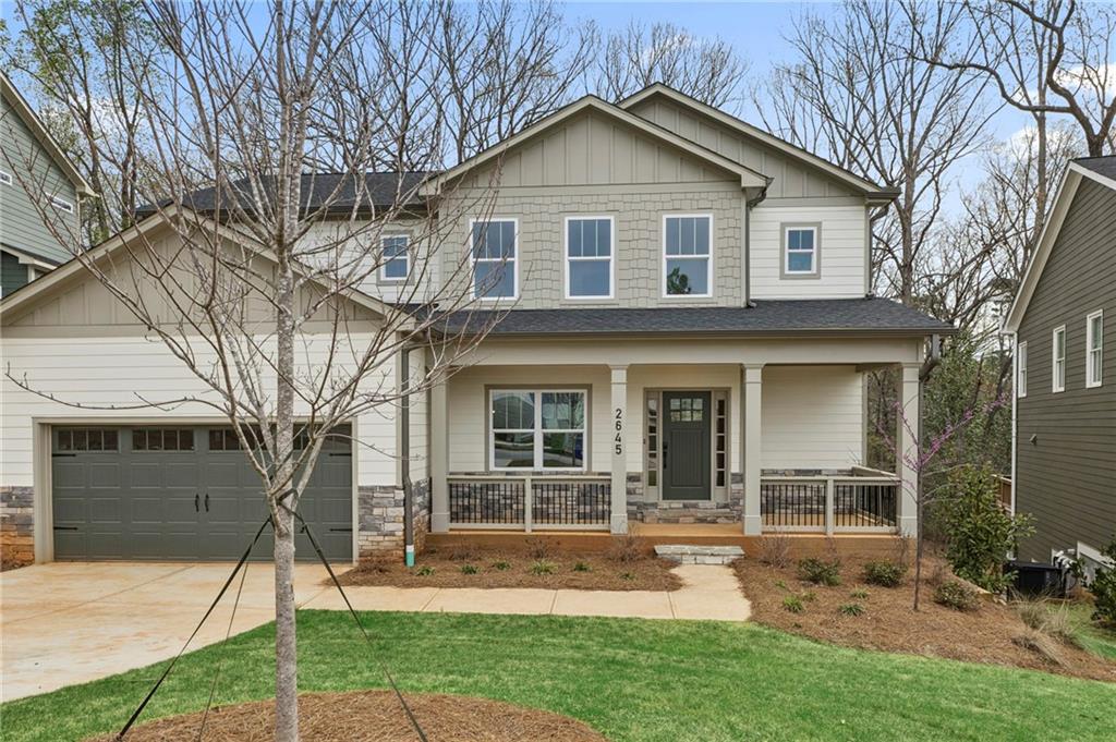 Craftsman-style house with covered porch, stone siding, driveway, and a front lawn