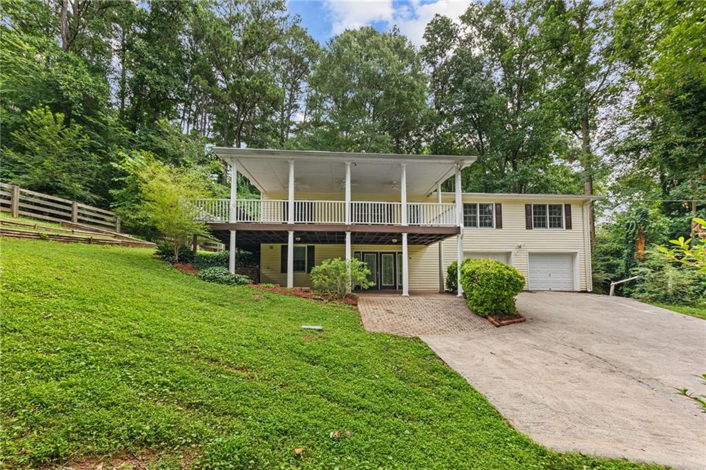 Split-level residence featuring a light-colored exterior, an upper-level covered porch with white railings, and a lower-level brick paver patio