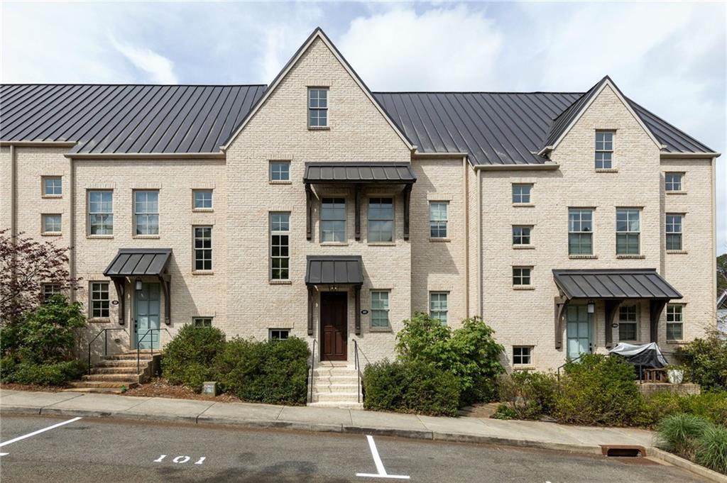 Multi-level townhome architecture featuring a light-colored brick facade, dark metal roofing, and multiple gables