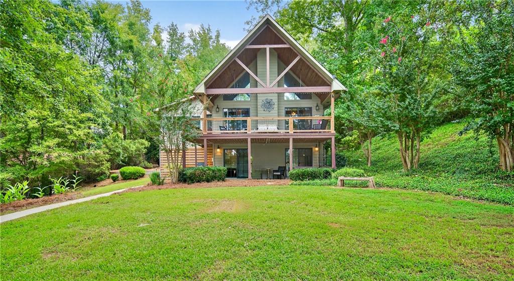 Tucked at the end of a private, shady driveway in the desirable Bluegill community, resides a rare opportunity on Lake Sinclair. With 162 feet of shoreline, a brand-new seawall, and wide open views across a quiet part of the lake, this stunning south-facing home enjoys the benefits of the lake's stunning sunrises and sunsets while the calm water is perfect for swimming, boating, fishing or just relaxing. The outdoor setting is exceptional: huge deck overlooking a manicured lawn, basement terrace and shuffleboard court make for fun family lakeside living. The covered boat dock includes a lift for your boat and wave runner, while the driveway has two powered outbuildings for storing gear or creating a hobby space. Inside, the home blends classic charm with modern comfort. The main floor features soaring A-frame windows that frame the lake and open onto the covered deck. The newly enclosed, climate-controlled sunroom functions beautifully as a dining or sitting room. An oversized primary suite resides on the main level, while the loft bedroom with its own full bath is perfect for company or can be used as an office. The finished basement level offers a second living space with a full kitchen, two bedrooms, and a full bath all opening onto the private lawn. Perfect for guests, extended family, or entertaining. With 2,483 sq ft, 4 bedrooms, and 3.5 bathrooms on nearly 3/4 of an acre, this home delivers space, privacy, and style in one of Lake Sinclair's most peaceful settings.