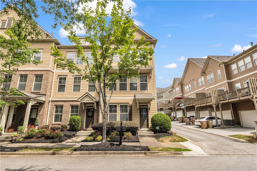 Three-story townhome featuring a brick facade with light-colored siding, a covered entry, and a small front yard with mature landscaping