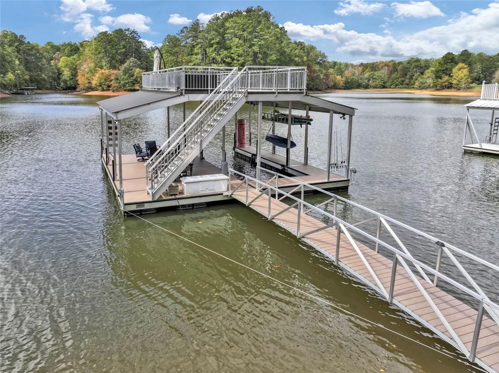 Serenity on the Lake: Luxurious Lakefront Escape. Unwind in upscale comfort at this beautifully updated 4-bedroom retreat on Lake Lanier.
Featuring a fully furnished lake home with hot tub, double-deck dock, and sweeping water views, on a private cove that is perfect for paddle boarding, fishing, and hanging out with your family. Calm water 99% of the time, plus the party top dock is always in deep water. Home is being sold fully furnished!
This home features a daybed swing front porch overlooking a beautifully landscaped front yard with river rock walls. Walk inside to a two-story foyer with rich wood stairs, warm cedar walls, and rich pine flooring throughout, creating a warm welcome for family and friends. Walk through the foyer to a two-story great room and be wowed by the rocked fireplace, beautiful cedar log walls, exposed beams, and rich tongue-and-groove ceiling. Turn around to see an open bridge connecting the master suite to an open loft area with built in bunk beds. The kitchen features granite counters, stainless steel appliances, LED lighting, and plenty of cabinet storage. The great room opens onto a large screened porch with breathtaking lake views and a grilling deck to the side. There are two bedrooms on the main level and a walkout to the back porch. A full bathroom with a tub/shower and a half bathroom complete the main level. The upper level features a large master bedroom with a walkout sitting porch overlooking the lake. The master bathroom has a spacious tiled shower and a luxurious jetted soaking tub overlooking the front forest. Walk back across the connecting bridge to the open loft area, suitable as an overflow bedroom, playroom, or office. The home sits on a full finished terrace level that includes another beautiful bedroom, huge bathroom with walk in shower, open game room and living area, web bar, cabinets, and sitting area. From the terrace level, exit to an entertainment area with a new hot tub and seating. From there it's a gentle walk to a max size 32x32 double deck dock with single-slip, covered entertainment area, upstairs party deck, and even installed green lights for those that want to fish. The dock has an end depth of 13.5 feet and has always been in deep water. Rip-rap installation and new stairs lead to the dock.
Just minutes from Lake Lanier Olympic Park and downtown Gainesville, you’ll enjoy easy access to both adventure and relaxation.
Bring your boat and loved ones to make lasting memories. Home is being sold fully furnished!