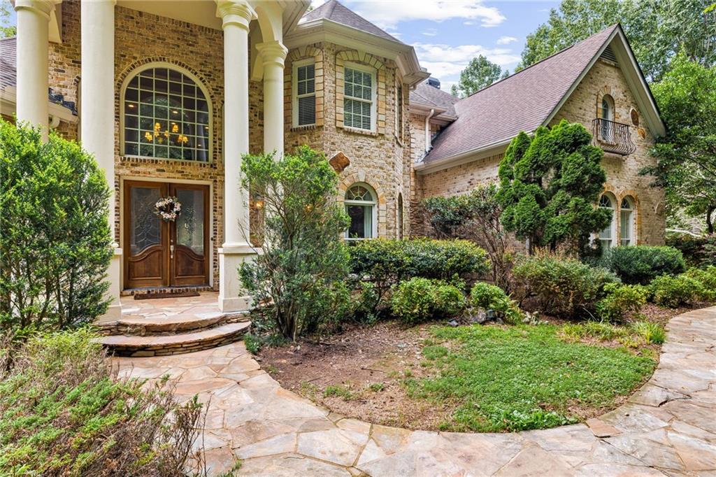 Welcome to this magnificent European-inspired estate, set on 3.64 private acres behind your own gated entry, yet just minutes from the charm and convenience of downtown Crabapple. Nestled at the end of a quiet cul-de-sac, this 5-bedroom, 5.5-bath residence has been thoughtfully designed with distinctive European styling. Exquisite woodwork, soaring ceilings, arched windows, marble and hardwood floors, and multiple balconies all combine to create a timeless elegance.
Through stately double wooden doors, you are greeted by an expansive marble foyer that immediately sets the tone for the home’s romantic beauty. To the right, graceful columns frame the dining room, while to the left, French doors open to a richly appointed office with walls of windows. Moving forward, the two-story great room impresses with floor-to-ceiling bookshelves showcasing intricate millwork and breathtaking views of Allmond Lake through its tall windows.
The chef’s kitchen is a work of art, featuring hand-painted and glazed cabinetry, granite countertops, stainless steel appliances, and a large island with sink—perfect for both cooking and gathering. An adjoining living area, complete with a wet bar and glass shelving, makes entertaining seamless. A charming bay window nook invites casual dining, while the nearby den offers a warm space to host family and friends. The main level also includes two private ensuite bedrooms, a powder room, and access to both the garage and basement. Up the graceful spiral staircase, a catwalk overlooks the great room below. The oversized owner’s suite offers a private retreat with space for a sitting area, direct access to a balcony, and a spa-inspired bath behind double doors. Here you’ll find a whirlpool tub, a separate shower, and abundant space to unwind in luxury. Every corner of this home has been lovingly cared for, and its exceptional design makes it feel as though you’ve escaped into a secluded European countryside retreat—yet all the conveniences of modern living are close at hand.