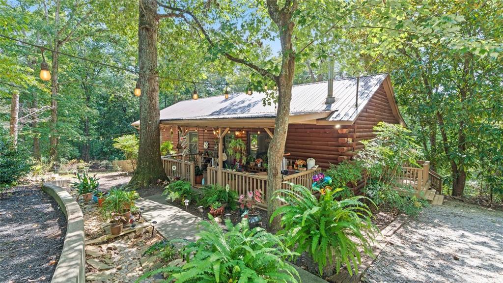 Escape to this enchanting renovated Log Cabin cottage situated minutes from Reinhardt University on 5 private wooded acres! Get away to your own mountain like retreat in this charming 2 bedroom 2 bath open concept home, complete with 2 new bathrooms and new kitchen. The energy efficient structure is an integrated log Cabin design with metal roofing and new HVAC system and beautiful wide plank pine flooring. The main area around the house is fenced and the beautiful natural setting, enhanced with flowering landscape plantings and lighting, leads to the large covered rocking chair front porch. Enter the spacious great room which is the heart of the home, with vaulted ceiling, open kitchen , sitting room with cast iron wood burning stove and dining area. Main hallway leads to secondary bedroom and new full bath with custom barn door. New owner's suite with spacious bedroom and sumptuous new full bath with soaking tub, and separate shower. Back hallway includes laundry room, built in shelving for pantry and storage, back door leads to huge back deck overlooking peaceful wooded back yard, and additionally a long side porch perfect for morning coffee and relaxing evenings. There are 3 separate outbuildings that serve the property. The first is an open covered grilling and smoker structure, great for the outdoor gourmet. The second is a large storage building with space for all you storage needs, and the third is a well equipped planting shed with clear ceiling panels to allow daylight for garden plantings. Completing this amazing property is a flower and vegetable garden area with wood pallet fencing. With 5 absolutely beautiful wooded acres, there are endless possibilities that make 502 George Gray Lane the perfect property for exceptional family living and entertaining!