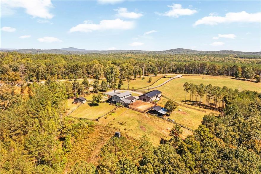 ?? One-of-a-Kind 12-Acre Farm Retreat
Welcome to a property that truly has it all — a rare blend of beauty, functionality, and endless possibilities. This 12-acre farm is unlike anything on the market, offering a custom barndominium that combines charm, versatility, and breathtaking views of both sunrises and sunsets.
Upstairs, you’ll find a bright and cheerful 3-bedroom, 2-bath home featuring a white kitchen with granite countertops, stainless-steel appliances, and a cozy keeping room anchored by a stone fireplace. The spacious family room opens to multiple decks overlooking rolling pastures, perfect for morning coffee or evening gatherings as the sky puts on a show.
The main-level in-law suite offers complete independence with its own kitchen, bedroom, and full bath — ideal for multi-generational living. A separate studio-style apartment provides even more flexibility, with a kitchenette, luxurious bath, and private covered deck overlooking the lush gardens — perfect for guests, rentals, or a home office.
The massive workshop is a dream come true — fully set up for work, hobbies, or entertaining with four garage bays, mounted TVs, storage, and even a hot tub area.
Equestrians will love the low-maintenance barn with four stalls, easy pasture access, auto-watering, hanging feeders, and stamped concrete for easy wash-outs. Under the home, you’ll find space for three additional stalls, bringing total capacity to seven. The property is fenced and cross-fenced, complete with irrigation, a drainage system, and plenty of parking for trailers, equipment, or guests.
Enjoy lush, green pastures, a peaceful creek, and private trails for horseback riding — and, with barrel racing next door for those who love the sport! And as if that weren’t enough, there’s a stunning pond and water feature with waterfalls, sitting rocks, and a beach-style area for relaxing on warm Georgia days.
This property can be the ultimate family homestead, multi-generational compound, or income-producing farm with three potential Airbnb opportunities. Located at the foothills of the North Georgia mountains, you’re just minutes from Ball Ground and Jasper for great dining, shopping, and small-town charm.
? There’s truly nothing else like it — come see for yourself!