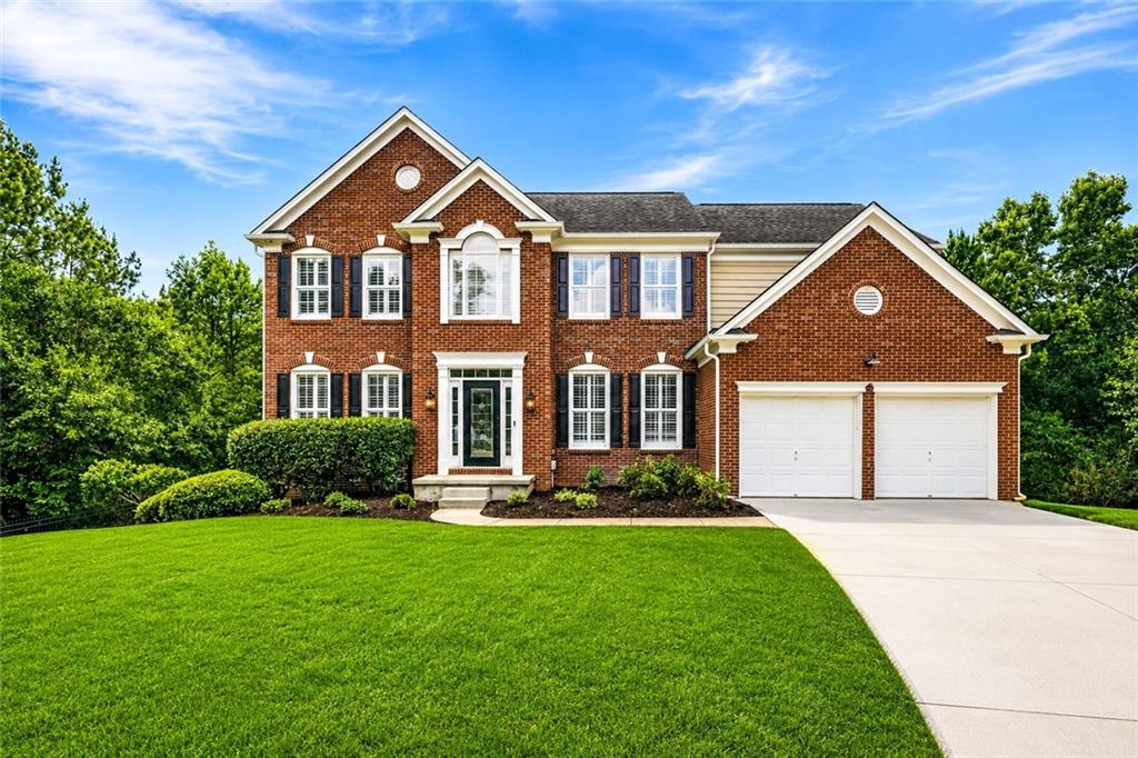 Brick facade residence featuring a two-car garage with white doors, a gabled roofline, and a prominent front entrance with sidelights