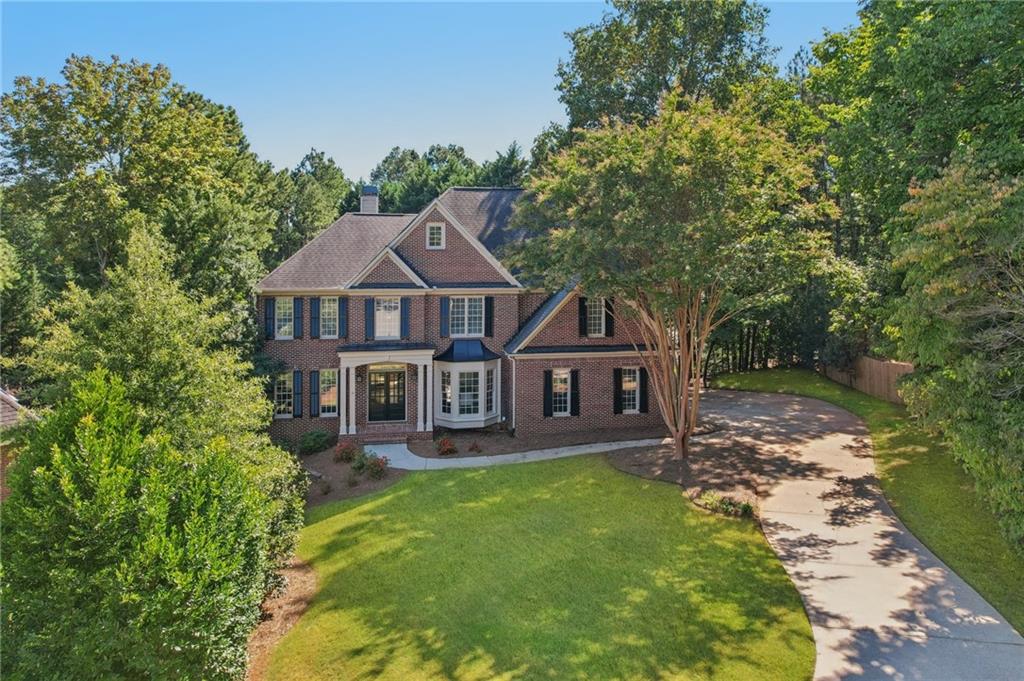 Welcome to this stately brick residence that blends timeless curb appeal with modern comfort. From the moment you arrive, the long driveway, lush landscaping, and classic front porch set the tone for a home designed for both elegance and ease. Inside, the soaring 2-story great room with its dramatic stone fireplace and wall of windows creates a stunning focal point, while the open layout flows seamlessly into the kitchen and breakfast area. With granite counters, stainless steel appliances, a center island, and abundant natural light, the kitchen is perfect for everyday living or entertaining.
The spacious primary suite is a serene retreat, featuring a sitting area surrounded by bay windows and a spa-like bathroom with dual vanities, soaking tub, and glass shower. Step outside to enjoy a private wooded backdrop from the covered deck or patio, ideal for relaxing afternoons. With thoughtful details throughout, generous living space, and a location in a desirable community complete with a playground, pool, racquetball, sidewalks, and tennis courts.