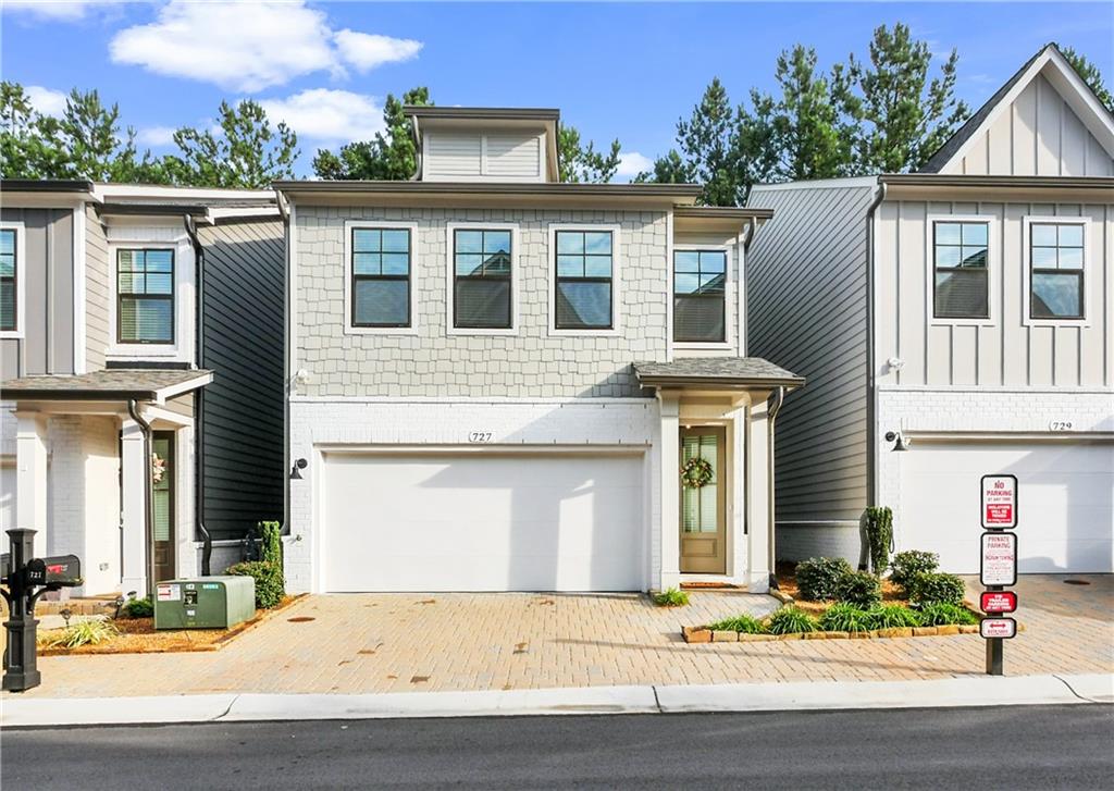 Modern townhome with a white brick facade, shake siding, black-framed windows, a covered entry, and an integrated garage