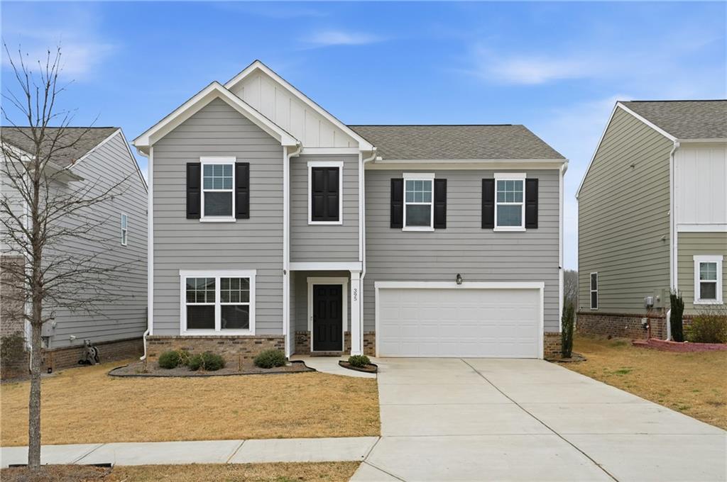 View of front of home featuring board and batten siding, an attached garage, concrete driveway, brick siding, and a shingled roof