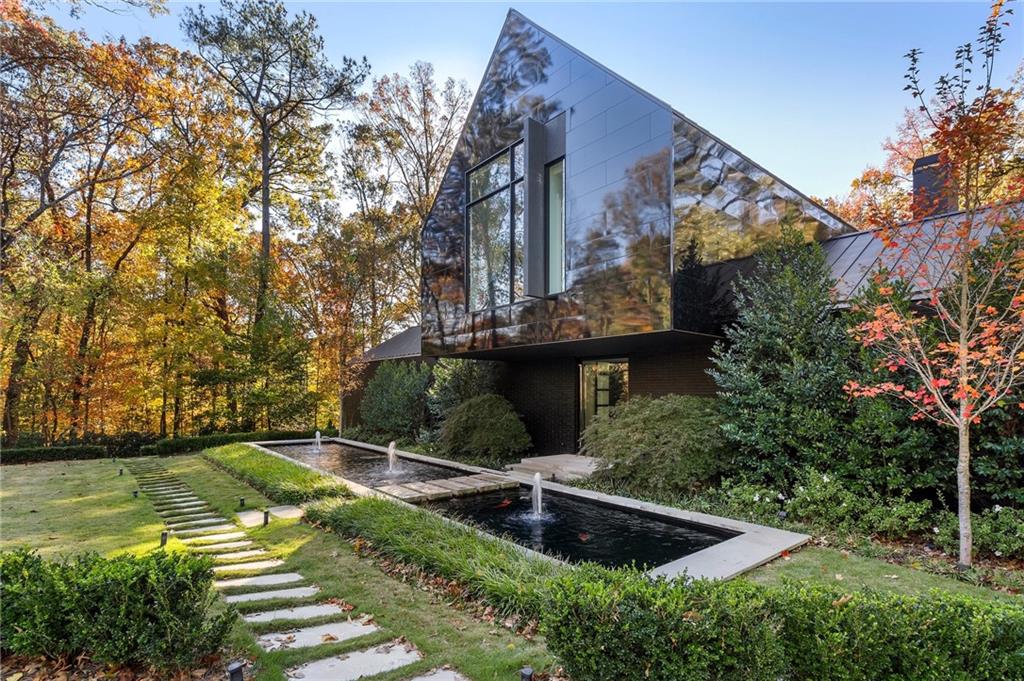 This exceptional Buckhead residence, thoughtfully designed by renowned architect Robert Tretsch III of Harrison Design, designed specifically for the lot (1.19 acres) that is also adjacent to protected land, Standing Fort Peachtree. The evolving landscape and koi ponds further enhance the design of this residence.  ADCO Builders and Harrison Design completed this residence in 2020 specifically as the Decorator Showhouse to commemorate the Atlanta Symphony's 75th Anniversary.  The exterior is Meridian brick and the black reflective wall panels, the first in the U.S. are Nichiha Miraia by Legendary Exteriors.  Upon arrival, guests are greeted by a striking water feature and koi pond and La Cantina glass pivot door. Stepping inside, the dramatic design unfolds to three stories of Windsor commercial-grade glass and steel frame with breathtaking views of the natural beauty of the property. The home's architecture is expertly oriented to capture optimal east-to-west exposure, flooding the interiors with natural light at every turn. The custom designed kitchen by Design Galleria features a 15 foot island in Temmer marble, custom cabinets by Kingdom, Wolf ovens and steam oven, Sub Zero and walk in hidden pantry.  Open to the family room with fireplace and doors out to a covered private patio. The dramatic dining room appears to float over the living room capturing views of the pool and property. The primary bedroom suite has floor to ceiling glass overlooking the pool. The bedroom features separate dressing rooms, a dreamy bath and quiet study with morning kitchen and an outdoor patio that overlooks the pool.  The expansive lower level is an entertainer's dream, featuring the main living room overlooking the 65 foot pool and featuring two fireplaces. The bar, theater and billiards are perfect for entertaining.  Two guest suites open directly to the pool area.  The upper level includes two additional bedroom suites and a second laundry room. Built with the latest energy-efficient systems, this home is equipped with Lutron controlled lighting, elevator and advanced technology for ultimate comfort and convenience. Nestled in the exclusive Paces Estate neighborhood-Buckhead's best-kept secret-this home enjoys a serene, tree-lined setting with minimum one-acre lot sizes, preserving both privacy and natural beauty. Conveniently located near Buckhead's top shopping, dining, and entertainment, and with easy access to the airport, this residence offers the perfect combination of luxury, tranquility, and proximity to city amenities.