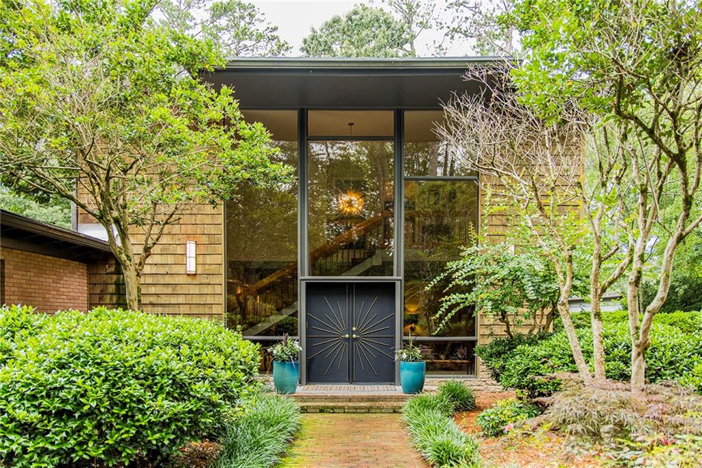 Step into timeless elegance with this stunning 1956 mid-century modern home, thoughtfully renovated to preserve its architectural heritage while offering today's luxury. Tucked away on 1.36 private, park-like acres along scenic Horseleg Creek in the historic College Heights neighborhood, this five-bedroom, four-bathroom residence is a true showstopper. From the moment you arrive, you'll be captivated by the striking two-story windows and custom sunburst-design entrance doors-an homage to the home's original 1950s styling. Inside, a dramatic open staircase with polished wood railings anchors the foyer, showcasing the sophistication of true mid-century architecture. A glamorous sitting room with a wood burning fireplace sets the tone when you enter, while the light-filled kitchen features a sunny breakfast area and flows seamlessly into the wood-adorned dining and living rooms. The living room is expansive and welcoming, with a beamed ceiling, gas log fireplace, and walls of windows that invite the lush natural surroundings inside. The main-level owner's suite is a serene retreat, complete with a spa-like bathroom offering a soaking tub, walk-in shower, and dual vanities. A versatile bonus space with a wooden ceiling-perfect for a home office, sunroom, or yoga studio-extends from the suite and opens onto a private deck. Two additional bedrooms and a full bath are also located on the main floor. Upstairs, two spacious suites each enjoy their own beautifully appointed private bathrooms, offering comfort and privacy for family or guests. Outside, entertain with ease around the fire pit, dine al fresco in the courtyard, or simply enjoy a quiet morning surrounded by nature. A detached two-car garage adds convenience and extra storage. With its impeccable renovation, classic lines, and rare setting, this home is more than a place to live-it's a legacy.