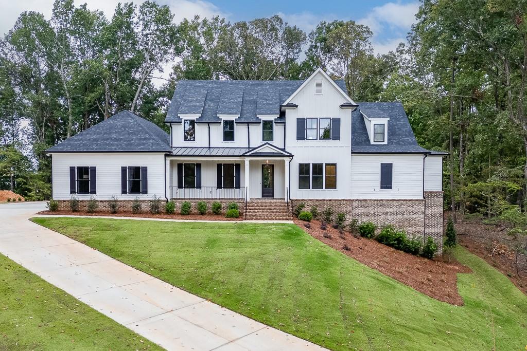 Modern inspired farmhouse with a front yard, a porch, a shingled roof, and view of scattered trees