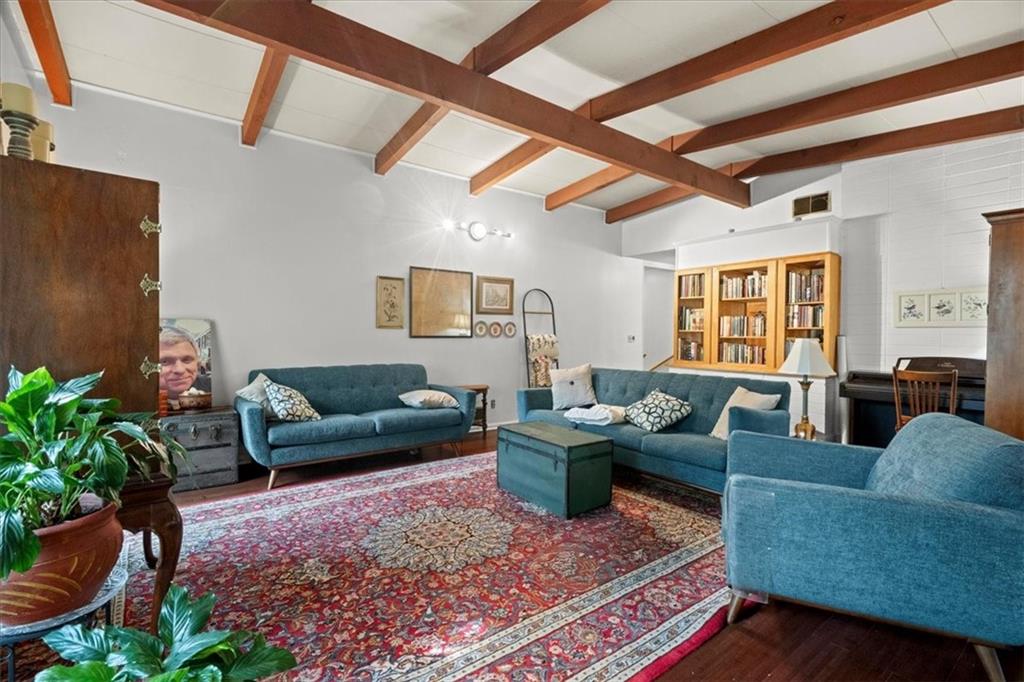 Living area featuring vaulted ceilings with exposed wood beams, built-in wooden bookshelves, dark wood-finish flooring, and white walls