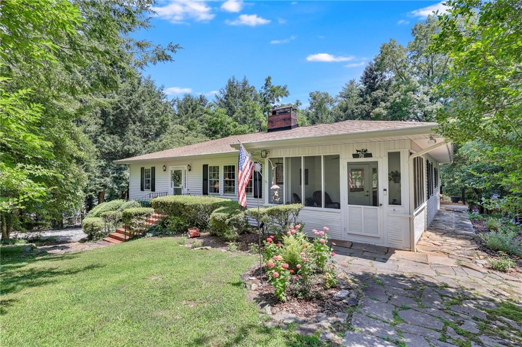 This beautifully updated 3B, 2BA home is tucked into a lush, wooded setting just a short stroll from the heart of downtown Clarkesville. With the vibrant town square just minutes away, you'll love everything about this peaceful retreat with unbeatable walkability. Step onto the classic flagstone path and you're greeted by a cheerful porch perfect for morning coffee or evening conversations. The immaculately landscaped yard bursts with color-blooming flowers, manicured shrubs, and mature trees offer privacy and natural beauty, completing the picture of timeless Southern charm. The open kitchen is a true showstopper, featuring quartz countertops and a generous center island. Crisp white cabinetry paired with stainless steel appliances, a wall of windows flooding the space with natural light, make this cozy breakfast nook overlooking the peaceful backyard the perfect place to start and end your days. 3 Gas Fireplaces, Hardwood floors, plantation shutters, and custom accents throughout reflect tasteful upgrades. The home flows effortlessly with its split-bedroom layout, updated baths, and is ideal for both relaxing and entertaining.