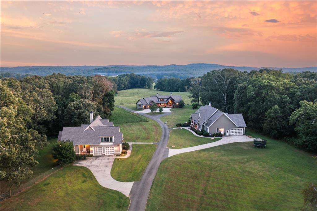 Nestled in picturesque Gilmer County, this sprawling 122± acre cattle farm in Ellijay boasts two beautiful homes, peaceful rolling hill pasture, a meandering creek and pockets of dense hardwood thickets. The three-bedroom, two-and three-half-bathroom main house boasts an inviting covered front porch that opens to a two-story foyer. The gourmet kitchen includes rich wood cabinetry, granite countertops, stainless steel appliances and a large island with a breakfast bar, which is all open to the dining area and has a vaulted living room. Floor-to-ceiling windows frame the property's stunning views, while a wood-lined cathedral ceiling and a stone fireplace flanked by built-ins add warmth to this large, welcoming keeping room. Two sets of French doors open to the covered porch, complete with an outdoor fireplace, a TV hookup, access to the screened porch and a half pool bathroom. Unwind in the spacious primary suite, which boasts a beamed cathedral ceiling, porch access, dual walk-in closets and a luxurious en suite bathroom with separate vanities, a freestanding soaking bathtub and a shower with multiple showerheads. Two additional main-level bedrooms are connected by a Jack-and-Jill bathroom. Completing the main level are an enormous laundry room with extensive cabinetry and storage, a half bathroom and access to the three-car garage. Upstairs, enjoy a bonus loft space with a half bathroom and plenty of room for a sitting area, games or an additional sleeping area. Outside, soak up the sun by the large saltwater pool, a spa with a waterfall feature and a diving board- all fenced and overlooking the verdant grazing grounds. The second home on the property sits on 3 of the 122 acres, and offers incredible living space with three bedrooms and three bathrooms. Enter from the covered front porch into the open floor plan layout. The large family room features a stone fireplace, a cathedral ceiling and access to the fireside rear screened porch. The adjoining dining space flows directly into the kitchen, which includes an island with seating, granite countertops, stainless steel appliances and timeless neutral cabinetry.  The pristine hardwood floors continue into the sleeping quarters, which include a tranquil primary suite with an en suite bathroom and two en suite guest rooms. The laundry room provides a utility sink, built-in storage and a drop-zone area to keep everything tidy. Upstairs, a large bonus room is perfect for a recreation room, office or additional bedroom. A two-car garage on the main level completes this immaculate home. The property includes various outbuildings/pole barns for hay and farm equipment storage, as well as a cattle barn and chicken shed. Located in the foothills of the North Georgia Mountains and just seven miles from downtown Ellijay, enjoy restaurants, wineries and charming retail stores, as well as Carter's lake just minutes from this breathtaking property! Experience the beauty, serenity and opportunity that await in beautiful Ellijay!