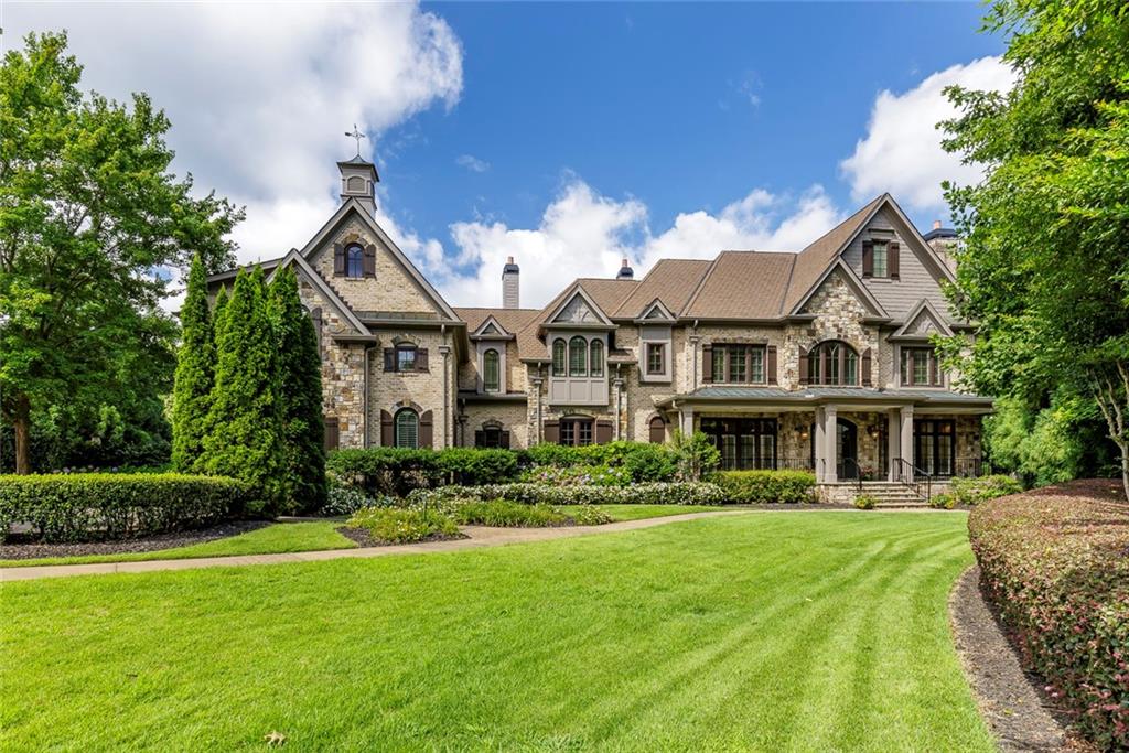 An extraordinary renovation in Johns Creek. Tucked away on a beautifully landscaped, 2.75-acre private lot, this spectacular estate has been completely reimagined by Barbara Dawes Designs, blending timeless architecture with bold, bespoke finishes and curated luxury at every turn. A grand two-story foyer welcomes you with a sweeping curved staircase adorned with iron railing, setting the tone for the artistry within. The formal dining room is anchored by a one-of-a-kind Alex Turco art installation titled “The World is Yours,” creating a conversation-starting centerpiece. The fireside family room offers architectural elegance with a coffered ceiling and a striking custom black leather marble mantel. A floating staircase adds to the home’s contemporary sophistication. Designed for chefs and entertainers alike, the kitchen is exceptional—featuring a custom pizza oven with artisan tile surround, a large island with quartzite countertops and farmhouse sink, and illuminated glass-front cabinetry showcasing your finest glassware. The culinary experience is elevated by top-tier appliances: a Wolf six-eye range with griddle and retractable Alex Turco backsplash, built-in SubZero refrigerator with dual freezer drawers, SubZero wine refrigerator, and Cove dishwasher. The adjacent scullery kitchen is equally outfitted with a True full-size refrigerator and freezer, Wolf cooktop with wok accessory, Wolf steam oven and warming drawer, Miele coffee system, Sharp microwave, second Cove dishwasher, craft paper dispenser, and custom walk-in pantry. Casual dining flows into a fireside breakfast area and into the keeping room, where NanaWall aluminum folding doors open to an exquisite three-season porch. This seamless indoor-outdoor connection features Bluestone flooring, fireplace, two Bromic outdoor heaters, and fully motorized vinyl shades and screens—creating the perfect year-round gathering space. Thoughtfully designed for everyday living, the main floor also includes a richly appointed library with built-in cabinetry and coffered ceiling, a fully custom mudroom with lockers, bench storage, and built-in planning desk. A dedicated dog room includes raised bathing area, pot filler, and built-in bowls. A spacious laundry room offers two sets of washers and dryers, floating shelves, custom cabinetry, and a farmhouse sink. A serene guest suite on the main level offers a luxurious retreat with Venetian plaster walls, a morning bar with beverage refrigerator, gas fireplace, and a spa-like bath clad in imported Carrara marble. The oversized open shower features dual rain heads and a soaking tub, complemented by a floating double vanity. Upstairs, the fireside primary suite is a true sanctuary with a private sitting area, morning bar, and lavish bath including heated floors, steam shower, soaking tub, dual vanities, two private water closets, and a vast custom closet. A flexible bonus room makes an ideal nursery, studio, or dressing space. Four additional en suite bedrooms are generously sized, each with custom finishes and elegant bathrooms. The finished terrace level extends the home’s luxury with a fireside media and lounge area, full bar, game room, exercise room, guest powder room, and spa bath with sauna, steam shower, and pool access. A secondary laundry room makes entertaining poolside effortless. Outdoors, enjoy resort-style living with a custom pool and spa, surrounded by a fully equipped outdoor kitchen including a built-in Evo gas grill, Eco flat-top griddle, Green Egg, and beverage cooler. A large, level grassy yard offers ample space for play, gardening, or entertaining. Every detail has been carefully considered—from brand-new 5/8" wire-brushed engineered hardwood flooring and wood beams to seven fireplaces and unparalleled finishes throughout. A rare offering blending craftsmanship, comfort, and designer flair in one of the most desirable and private settings.