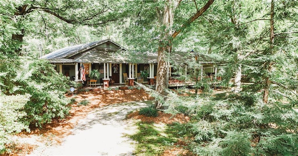 Discover this beautifully crafted cottage-style home that combines charm, comfort, and convenience. Ideally located just minutes from the interstate, schools, and local retail, this home offers the perfect blend of peaceful living and accessibility. Step onto the inviting covered wraparound porch and take in the mature landscaping that surrounds the property. A spacious deck extends from the porch, making it an ideal space for entertaining, relaxing, or enjoying the outdoors year-round. Inside, you'll find a bright, open interior filled with natural light and designed for functional everyday living. The thoughtful layout provides a seamless flow between spaces while maintaining the cozy, cottage feel. The exterior features well-maintained hardwoods, lush greenery, and multiple accessory buildings, including a 900 sqft metal garage on a concrete slab with roll up doors-perfect for storage, hobbies, or a workshop. Don't miss this unique opportunity to own a custom-built home that offers both character and convenience!
