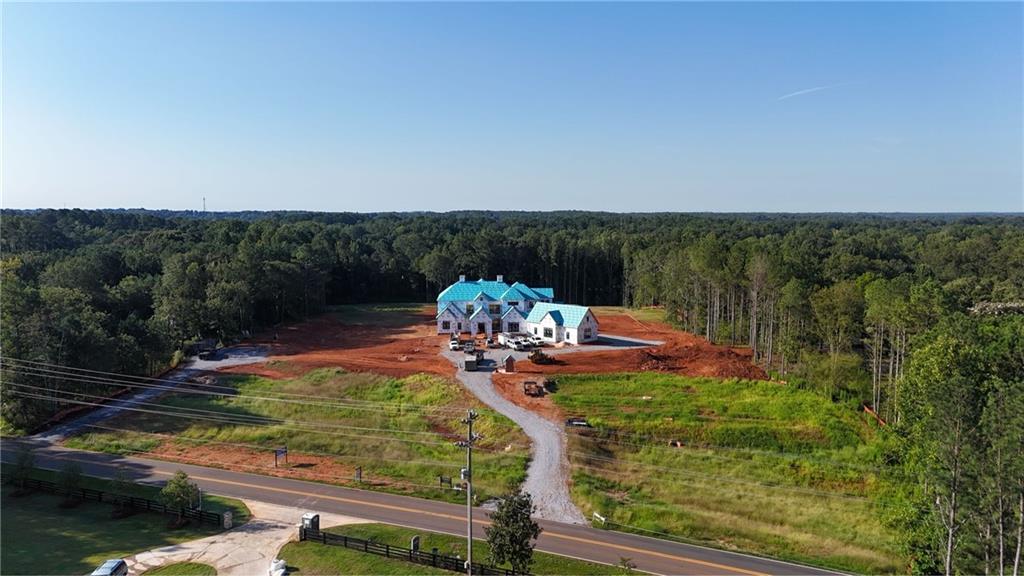 Set on over 12 acres in the heart of Milton, this private gated estate offers a rare blend of luxury, lifestyle, and land. Currently under construction by award-winning Loudermilk Homes, this custom-designed 11,000+ square foot residence features 5 bedrooms, 6.5 bathrooms, and a layout that brings together refined architecture with relaxed, everyday living in one of Georgia’s most sought-after communities.
This thoughtfully planned floor plan balances grand entertaining and personal retreat, beginning with a main-level primary suite that serves as a serene escape featuring a spa-style bath with dual oversized dressing rooms, and direct access to a covered terrace overlooking the resort-style pool and expansive grounds. At the heart of the home, a chef-inspired kitchen with double islands, a separate prep kitchen, walk-in pantry, and top-of-the-line Wolf and Sub-Zero appliances connects seamlessly to the living and dining areas, combining function and elegance in equal measure. The terrace level expands the experience with a full bar, poker room, fitness space, and multiple finished storage areas, while a state-of-the-art low voltage system integrates whole-house audio, home advanced security, and future-ready smart home capabilities. Upstairs features additional spacious bedroom suites with walk-in closets and en-suite baths, along with elevator-ready framing for long-term convenience. Expansive covered patios blur the line between indoor and outdoor living, with a custom pool perfectly positioned to capture the natural beauty of the landscape. A poured pad is already in place, offering future potential for a guest house, car barn, pool house, or equestrian facilities—allowing the property to evolve with your vision. From the moment you pass through the gates, the sense of arrival is undeniable—this is a home that lives as beautifully as it entertains. Whether you’re hosting large gatherings or enjoying quiet evenings under the stars,
every element has been curated with intention. Just minutes from top-ranked schools, local dining, and scenic parks, and less than an hour from both Buckhead and Hartsfield-Jackson Atlanta International Airport, this rare offering captures the essence of Milton living: elegant, timeless, and deeply connected to both community and land.