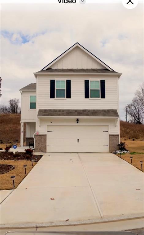 View of front of home featuring brick siding, board and batten siding, driveway, and an attached garage
