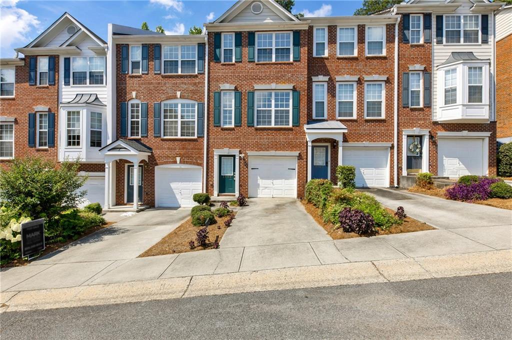 Brick townhome exterior featuring white-framed windows with dark blue shutters, a covered entry, and a single-car garage