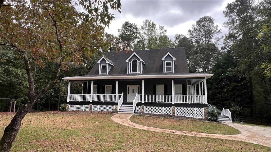 Farmhouse-style home featuring a front yard, a porch, and view of wooded area
