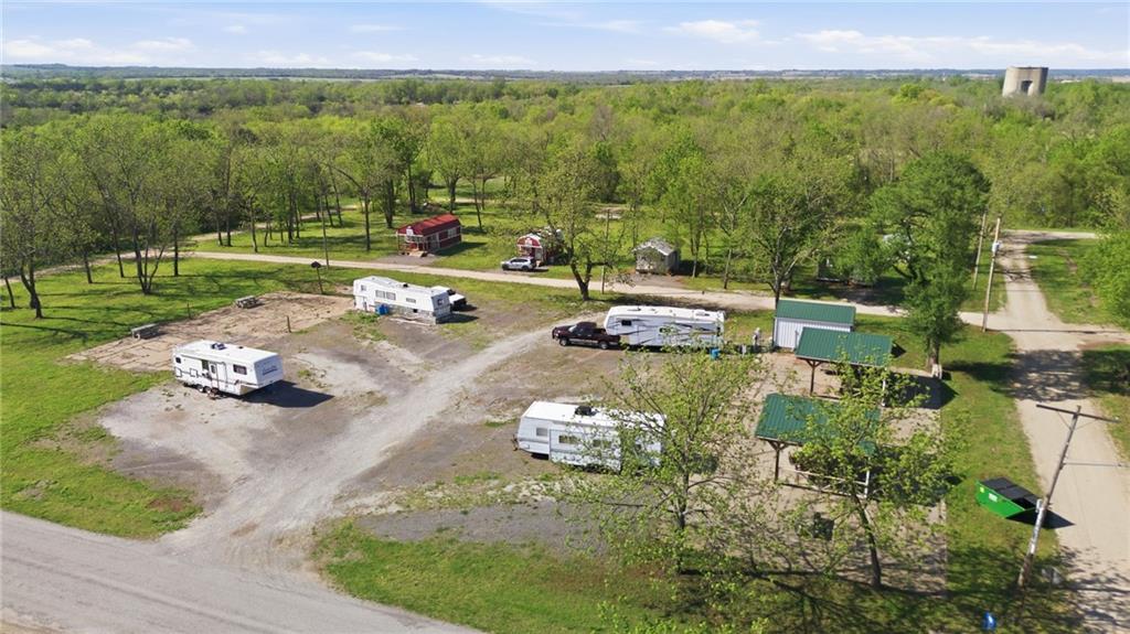 An aerial view showcasing a large property with a combination of gravel and grassy areas, surrounded by numerous mature trees